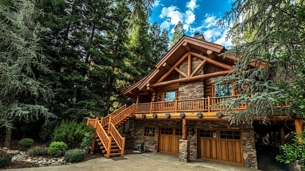 A log cabin with a stone foundation, a wooden deck, and a staircase leading to a balcony. - Luxury Log Cabin Home at Bass Lake with Air Conditioning, with backup generator  (Bass Lake)