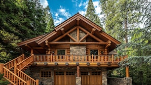 A log cabin with a stone foundation, a wooden balcony, and a staircase leading to the entrance. - Luxury Log Cabin Home at Bass Lake with Air Conditioning, with backup generator  (Bass Lake)