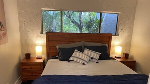 A bedroom with a large bed, two bedside tables, a window with a view of trees, and a textured wall.