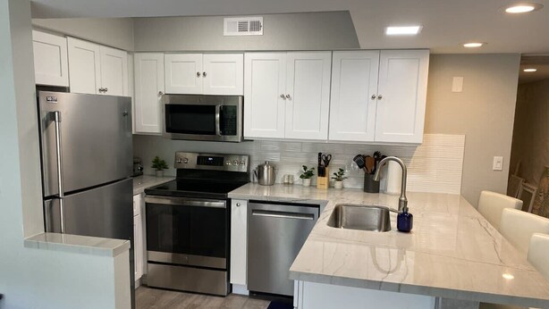 A modern kitchen with white cabinets, stainless steel appliances, and a marble countertop.