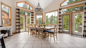 A spacious dining area with a large table and chairs, large windows, and a chandelier. - Chateau Lawrence | Pool Table | Kids` Gaming Room (Fairmont Hot Springs)