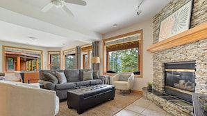 A modern living room with a stone fireplace, large windows, and a pool table. - Chateau Lawrence | Pool Table | Kids` Gaming Room (Fairmont Hot Springs)