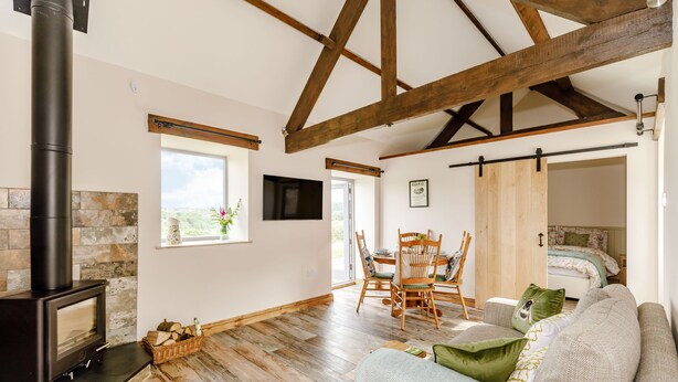 A cozy room with a fireplace, wooden beams, a dining area, and a bed. - Foxglove (Whitby)