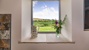A window seat with a view of a green landscape, a decorative pitcher, and a vase with flowers. - Foxglove (Whitby)