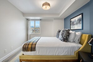 A bedroom with a bed, a window with curtains, a painting on the wall, and a ceiling light. - High Noon | Top Floor | Pool | Hot Tub | Gym (Invermere)