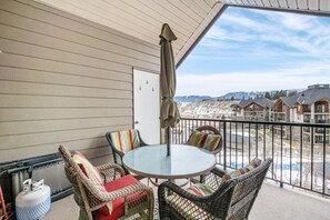 A balcony with wicker chairs, a round table, and a view of a snowy landscape. - High Noon | Top Floor | Pool | Hot Tub | Gym (Invermere)