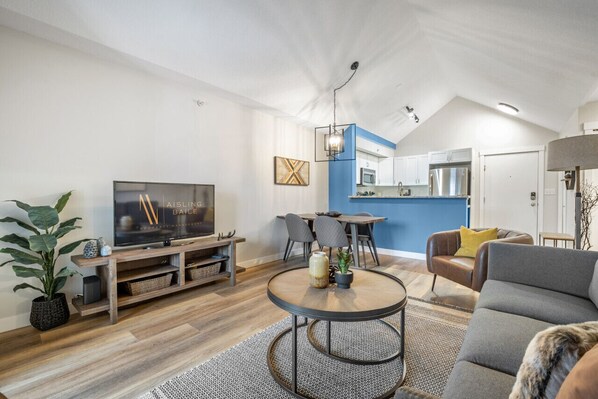 A modern living room with a TV, dining area, and kitchen. - High Noon | Top Floor | Pool | Hot Tub | Gym (Invermere)
