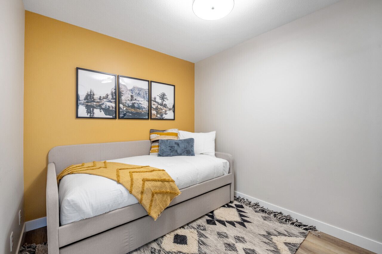 A bedroom with a bed, a yellow accent wall, and three framed pictures.
