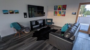A living room with a black leather sofa, a teal armchair, a flat-screen TV mounted on the wall, and a cowhide rug.