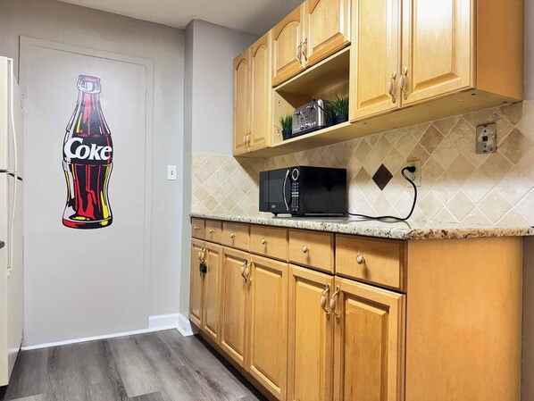 Compact kitchen with a microwave, toaster, and potted plants on a granite countertop.