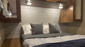 Une chambre à coucher de taille réduite, comprenant un lit, deux oreillers, une tête de lit et des armoires en bois.