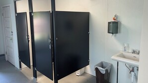 Des toilettes avec des cabines séparées par des cloisons noires, un lavabo blanc et une poubelle.