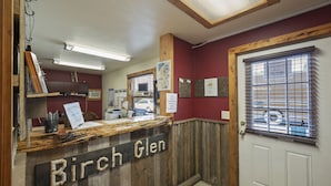 A reception desk labeled "Birch Glen" with a wooden design, a map on the wall, and a window with blinds. - Birch Glen Lodge (Cascade)