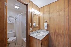 A bathroom with wooden paneling, a white sink, a mirror, and a shower curtain.