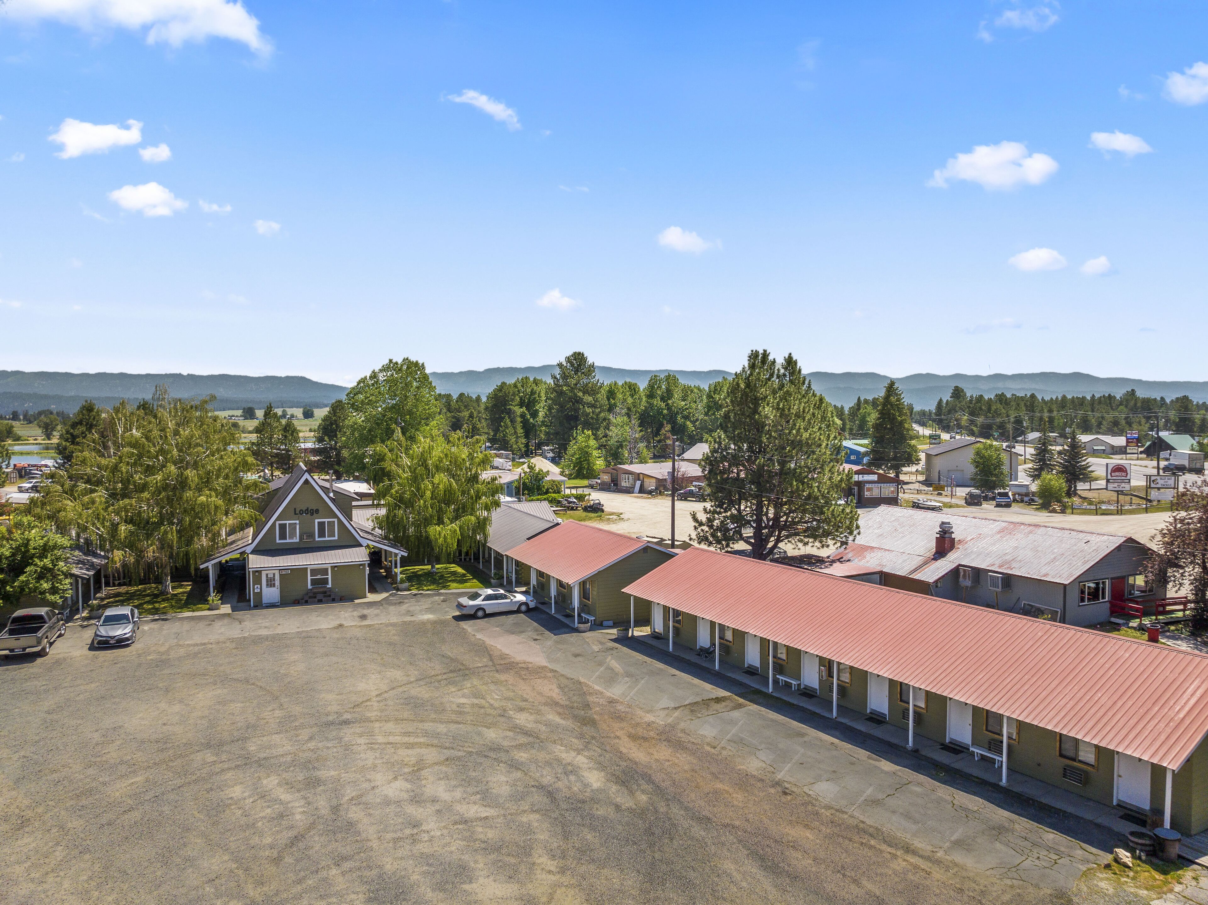 A motel with a red roof, a parking lot, and a view of mountains in the background.