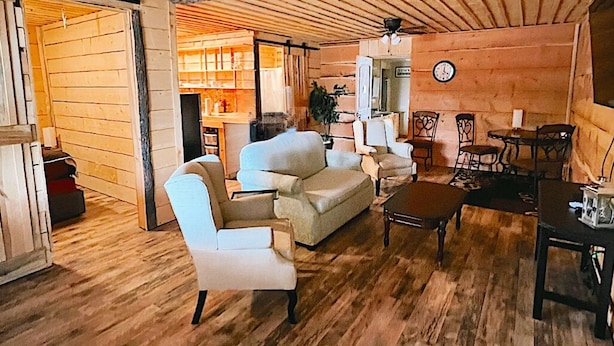 A cozy log cabin interior with a wooden ceiling, a sofa, armchairs, a dining table, and a clock on the wall. - Birch Glen Lodge (Cascade)