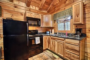 A kitchen with wooden cabinets, a black refrigerator, a microwave, a stove, and a coffee maker.