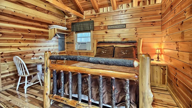 L’intérieur d’une cabane en rondins, avec un lit en bois, un bureau, une chaise et une fenêtre.