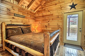 A wooden cabin interior with a bed, a star decoration, and a door leading outside.