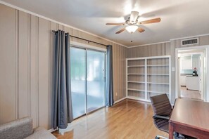 A room with a ceiling fan, a sliding glass door, a wooden floor, a brown leather chair, and a wooden table.