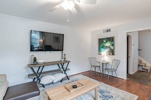A living room with a ceiling fan, a flat-screen TV, a coffee table, and a seating area with chairs. - Near Midtown, Highways, Downtown! Bel-Air Bungalow (Mobile)