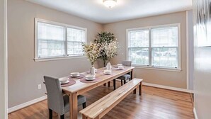 A dining area with a wooden table, chairs, and a bench. There are two windows with blinds, a ceiling light, and a wall-mounted artwork. - Near Midtown, Highways, Downtown! Bel-Air Bungalow (Mobile)
