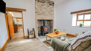 A cozy living room with a stone fireplace, wooden flooring, a sofa, and a table with fruit. - Torties Cottage (Brampton)