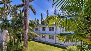 A two-story building with a white exterior and blue roof, surrounded by lush greenery and palm trees. - Renovated Studio at Naples Beach & Town! (Naples)