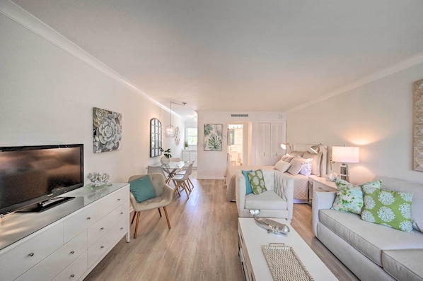 A modern living room with a flat-screen TV, a glass coffee table, a sofa, and a dining area with a table and chairs. - Renovated Studio at Naples Beach & Town! (Naples)