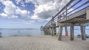 A beach with a wooden pier extending into the water, a sandy shore, and a clear sky with clouds. - Renovated Studio at Naples Beach & Town! (Naples)