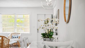 Un coin repas avec une table en verre, des chaises blanches, une orchidée en pot et un miroir encadré en bois accroché au mur.