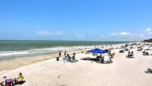 Une plage bondée où les gens se détendent sous des parasols et des tentes, et d’où l’on a une vue dégagée sur l’océan.