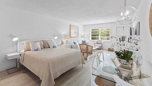 Une chambre moderne avec un grand lit, des tables de chevet, une table à manger en verre et un luminaire suspendu.