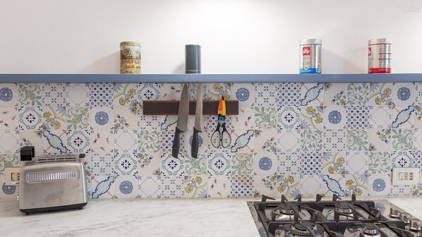 A kitchen with a tiled backsplash, a gas stove, a toaster, and kitchen utensils hanging on the wall.