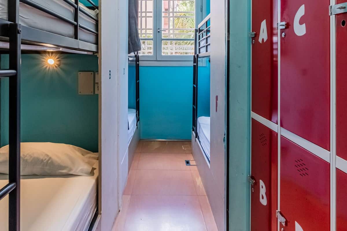 A narrow corridor with bunk beds on one side and red lockers on the other.
