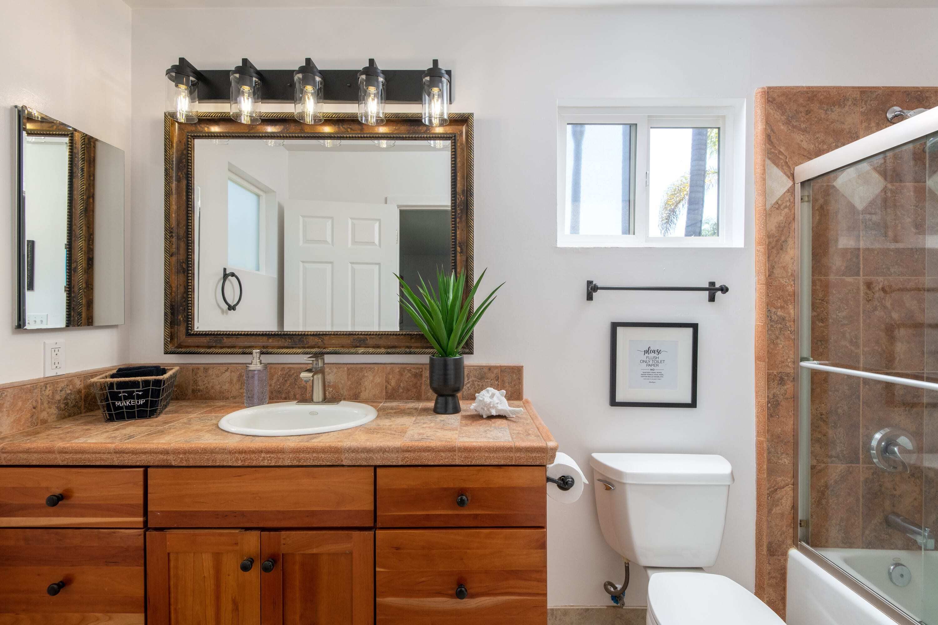 A bathroom with a wooden vanity, a large mirror with lights, a sink, and a shower area.
