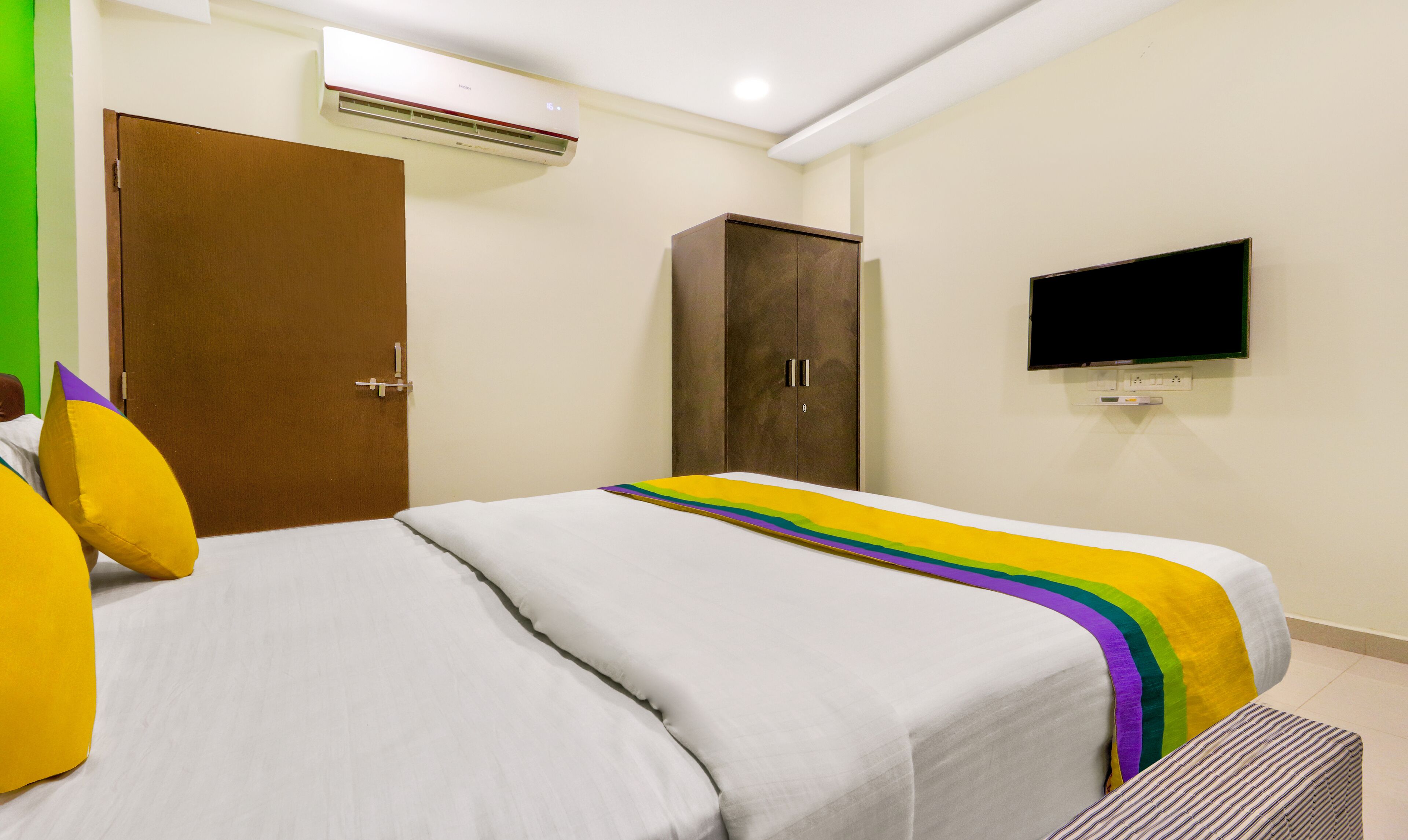 A hotel room with a bed, a wardrobe, an air conditioner, and a television.