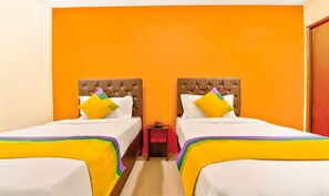 Habitación de hotel con dos camas, cada una con cabecera acolchada, ropa de cama blanca y almohadas coloridas.
