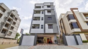 Un edificio residencial de varios pisos con diseño moderno, que cuenta con balcones, equipos de aire acondicionado y una entrada protegida por un portón.