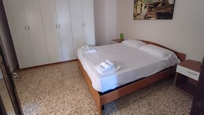 A bedroom with a bed, a wardrobe, a nightstand, a green lamp, and a painting of a bridge. - VILLA ROSA 2 - Antico Borgo Scopello NEAR THE SEA (Scopello)