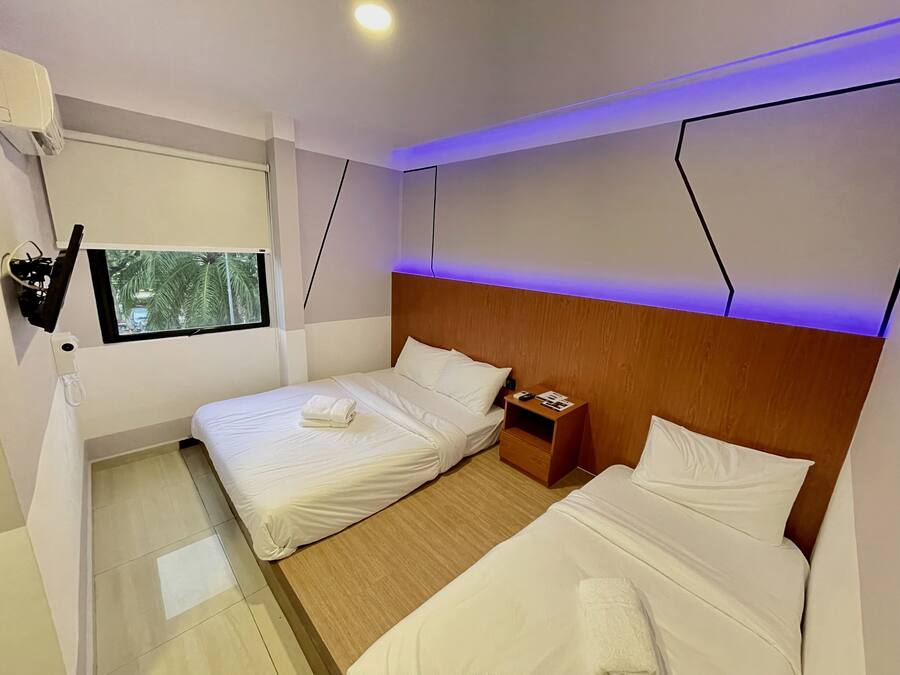 Habitación de hotel con dos camas, cabecera de madera, mesita de noche, ventana con vista a palmeras y televisor montado en la pared.