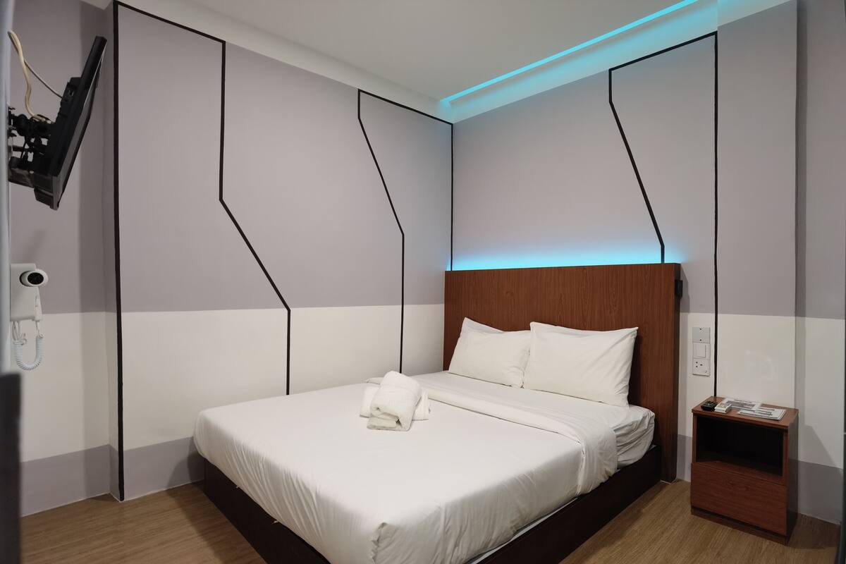 Ein modernes Hotelzimmer mit einem ordentlich bezogenen Bett, einem Holzkopfteil und einem Nachttisch mit Telefon und Papieren.