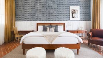 Un dormitorio con cama de madera, pared estampada, silla de madera y sofá de cuero marrón.