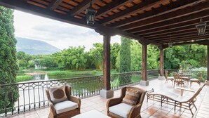 A covered outdoor seating area with wicker furniture and a view of a river and greenery.