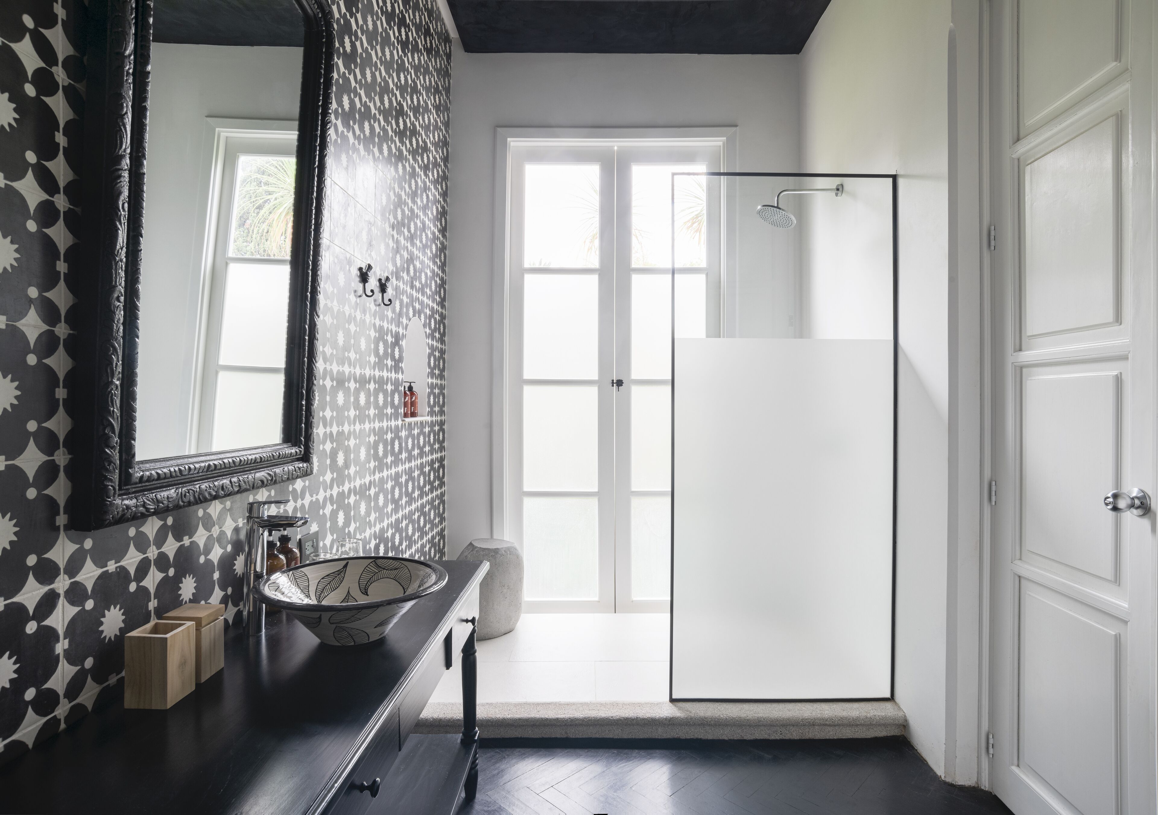 Ein Badezimmer mit großem Spiegel, Waschbecken, Dusche und einer Tür zu einem weiteren Raum.