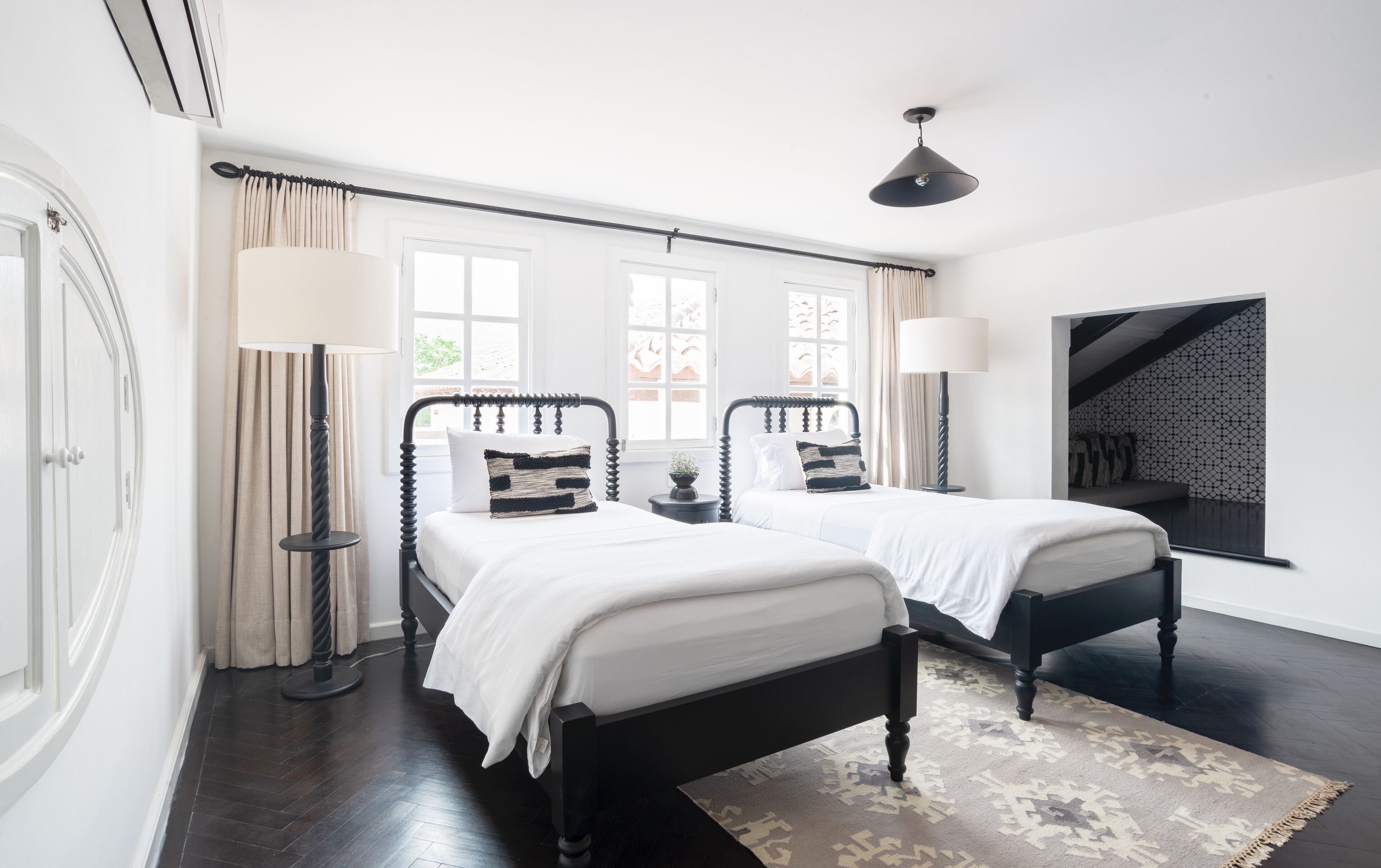 A hotel room with two beds, a large window, a ceiling fan, and a patterned rug.
