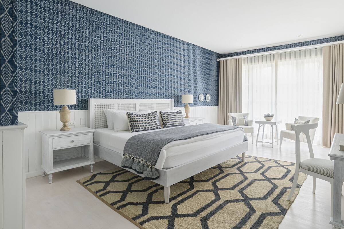 Quarto moderno com parede azul estampada, cama branca e tapete geométrico.