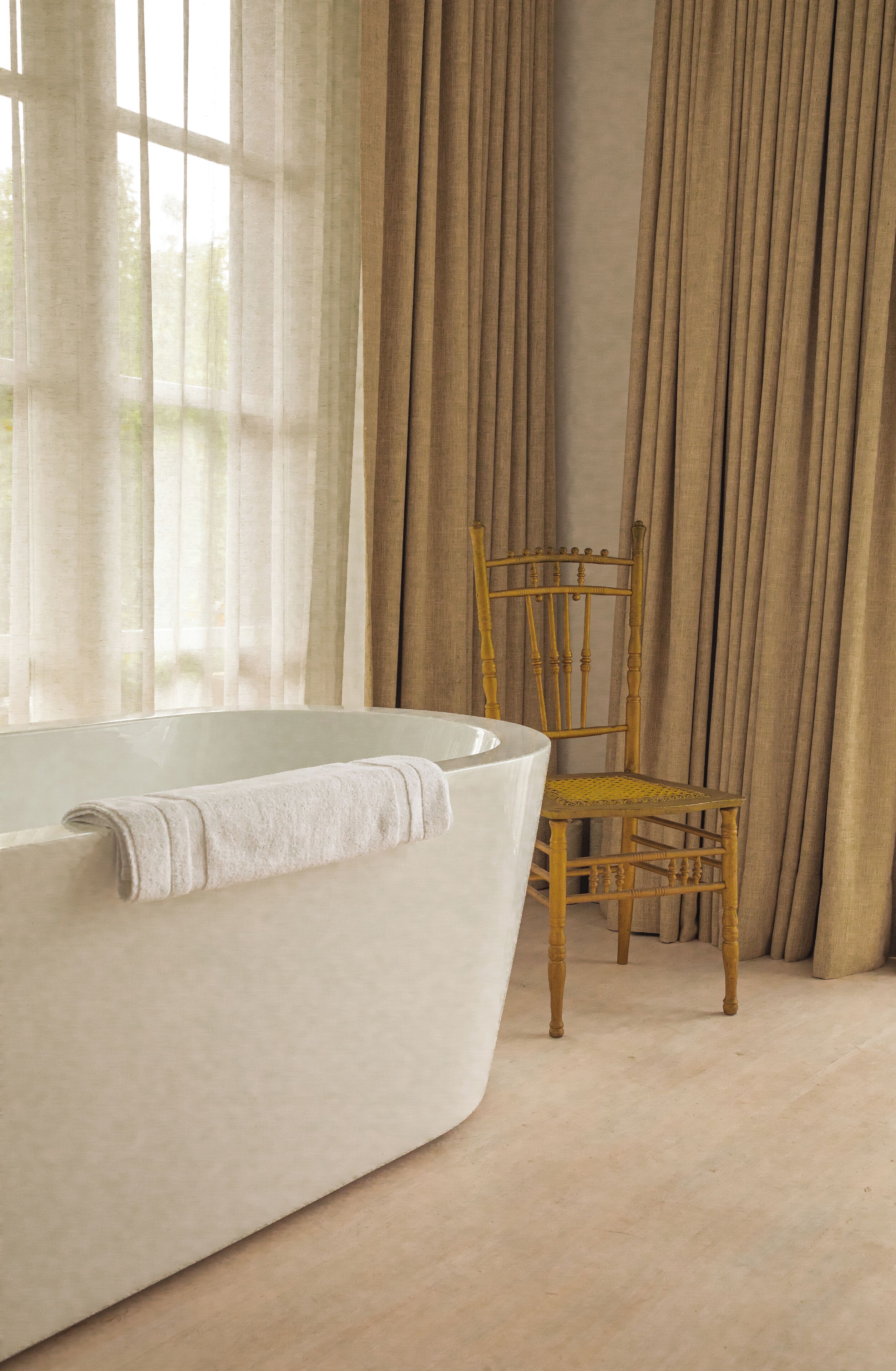 A bathroom with a bathtub, a wooden chair, and beige curtains.