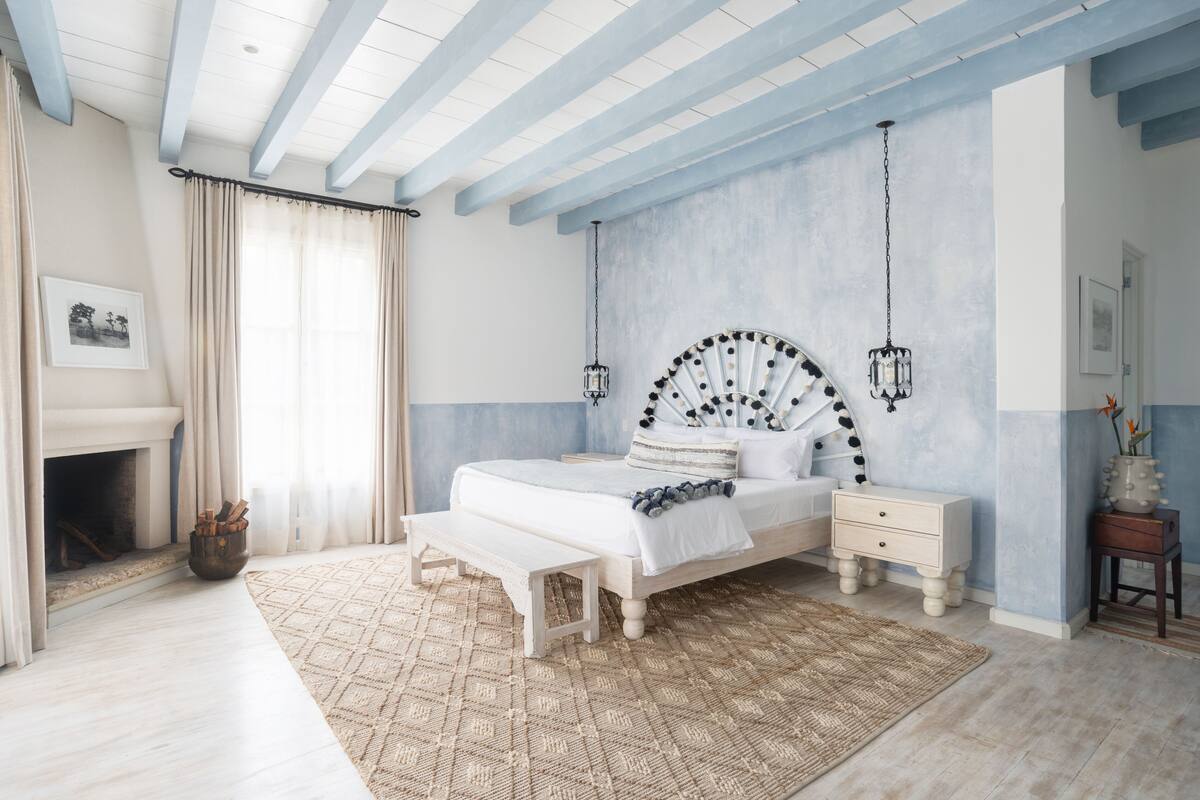 Quarto com cama, mesas de cabeceira, um aparador, lareira e luminária pendente.