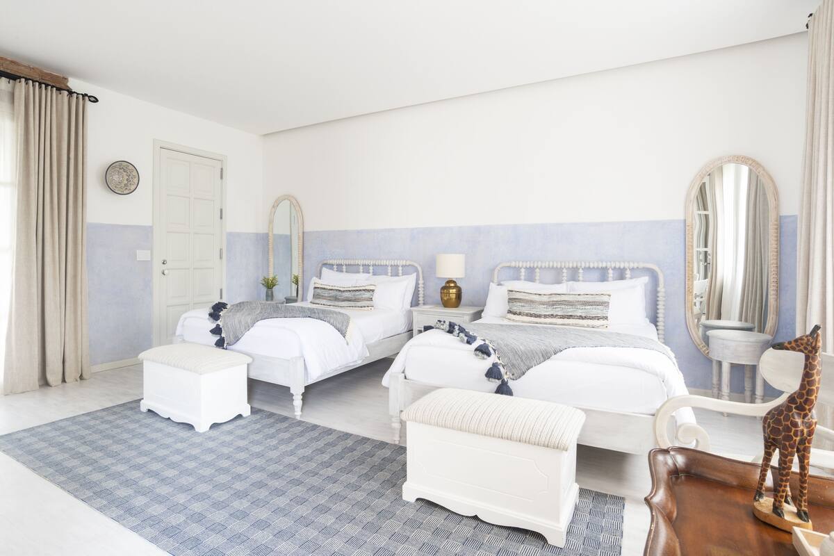 Quarto com duas camas, um espelho grande, uma escultura de girafa de madeira e um tapete estampado.